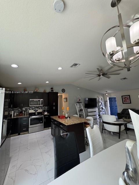 kitchen featuring a center island, vaulted ceiling, a textured ceiling, appliances with stainless steel finishes, and ceiling fan