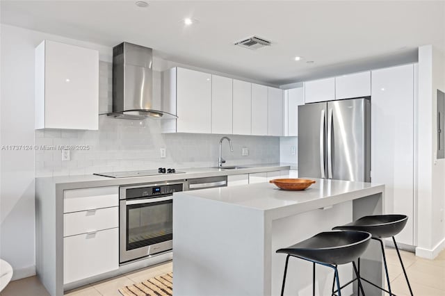 kitchen featuring sink, appliances with stainless steel finishes, white cabinets, a kitchen island, and wall chimney exhaust hood