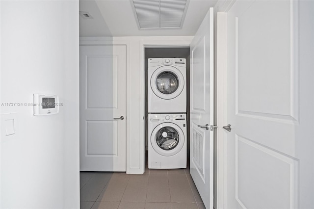 laundry area featuring stacked washer and clothes dryer and dark tile patterned floors