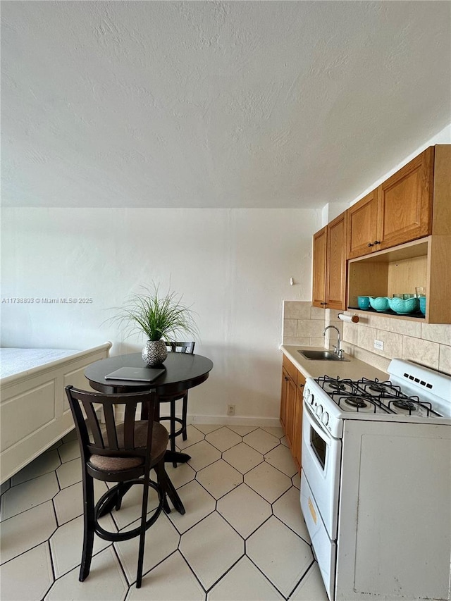 kitchen featuring a sink, light countertops, white gas range oven, brown cabinets, and backsplash