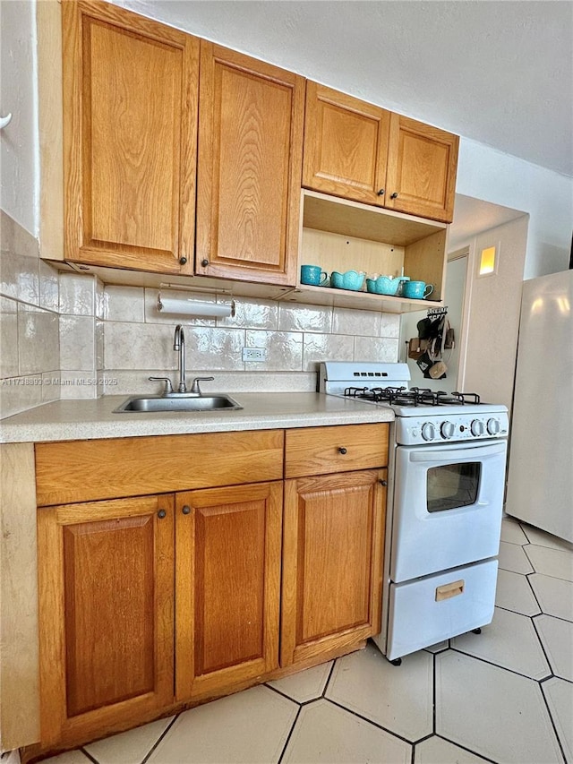 kitchen with backsplash, light countertops, white range with gas cooktop, freestanding refrigerator, and a sink