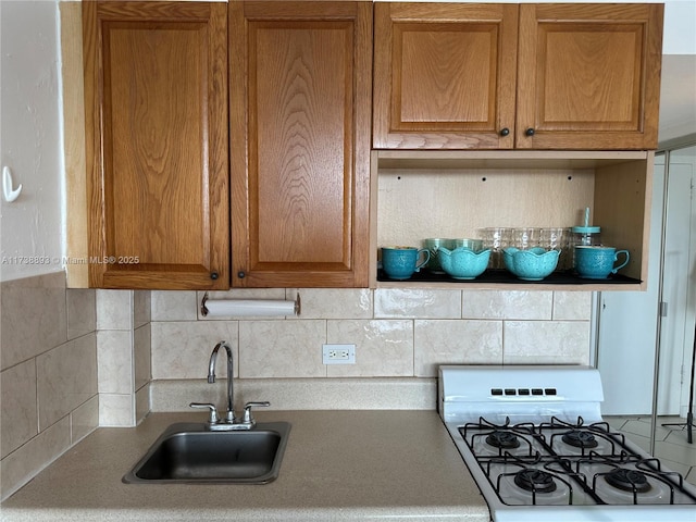 kitchen featuring white range with gas cooktop, brown cabinetry, backsplash, and a sink