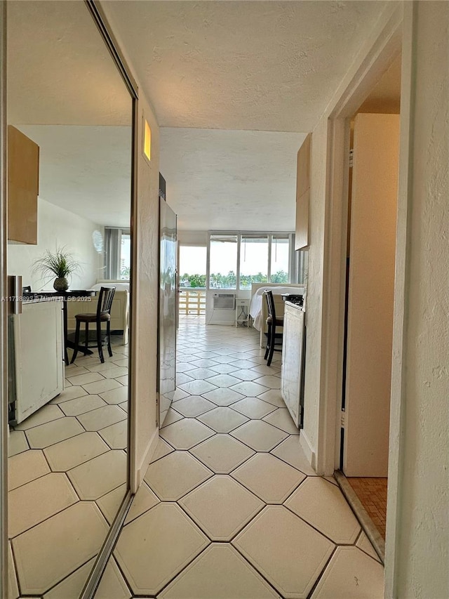 hall with a textured ceiling, a textured wall, and light tile patterned floors