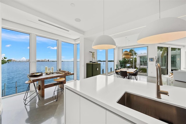 kitchen with pendant lighting, a water view, white cabinetry, and sink