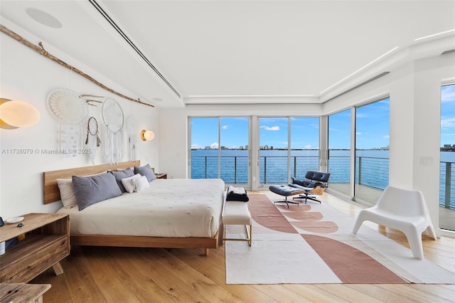 bedroom with a water view, light hardwood / wood-style flooring, and access to outside