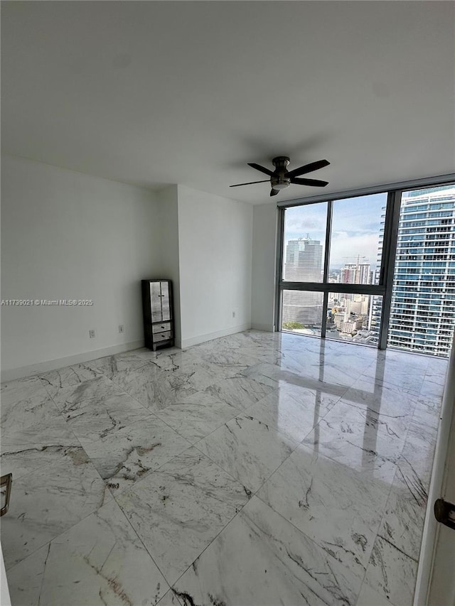 empty room with a ceiling fan, baseboards, marble finish floor, floor to ceiling windows, and a view of city