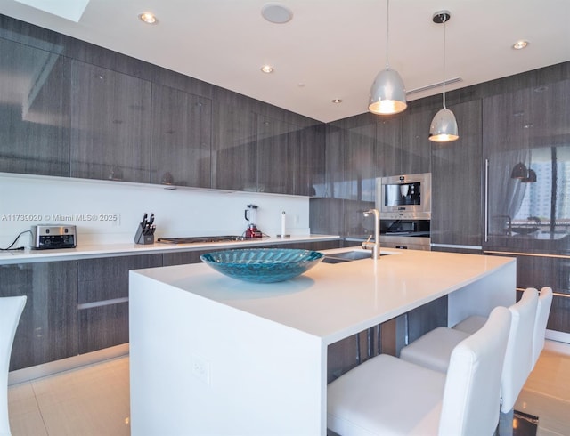 kitchen featuring sink, a breakfast bar area, hanging light fixtures, stainless steel appliances, and an island with sink
