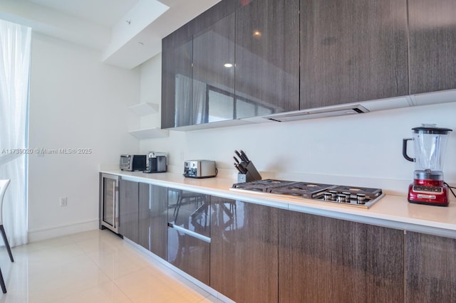 kitchen featuring light tile patterned flooring, wine cooler, dark brown cabinets, stainless steel gas stovetop, and exhaust hood