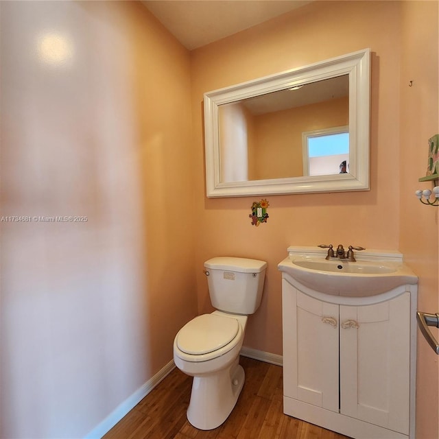 half bath with vanity, baseboards, wood finished floors, and toilet