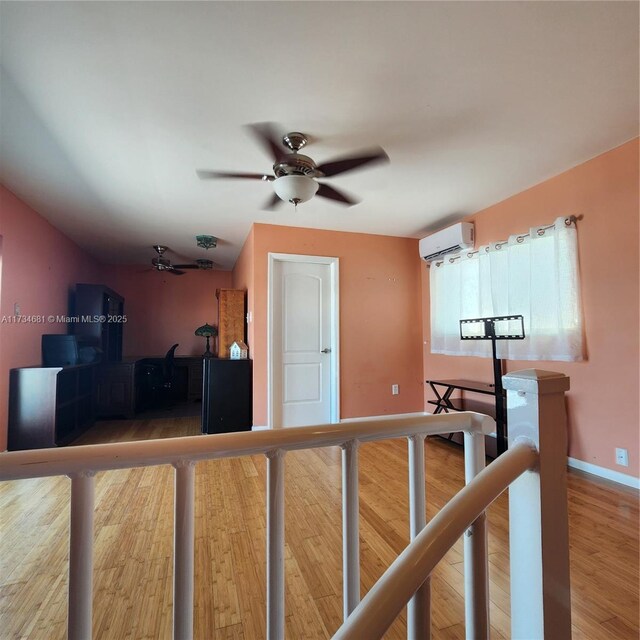 interior space featuring a ceiling fan, baseboards, a wall mounted AC, and wood finished floors