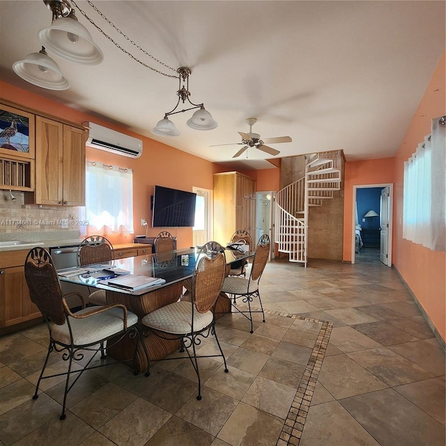 dining room with an AC wall unit, stone finish flooring, ceiling fan, and stairway