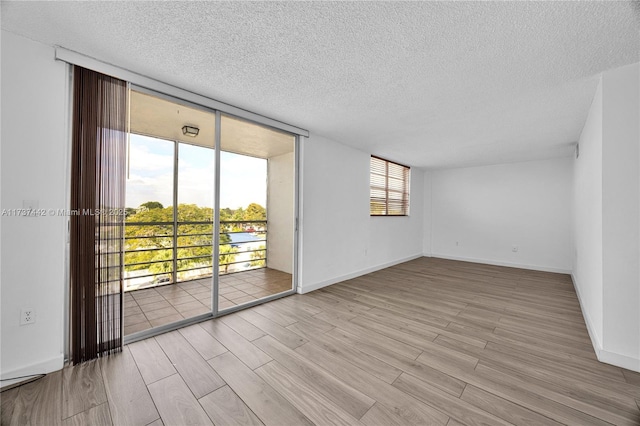 empty room with expansive windows, a textured ceiling, and light wood-type flooring