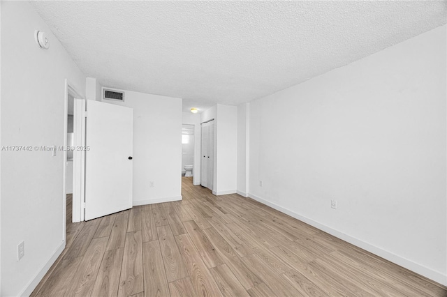 unfurnished bedroom featuring a closet, a textured ceiling, light wood-type flooring, and ensuite bath