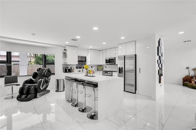 kitchen with a breakfast bar, tasteful backsplash, a center island, stainless steel appliances, and white cabinets