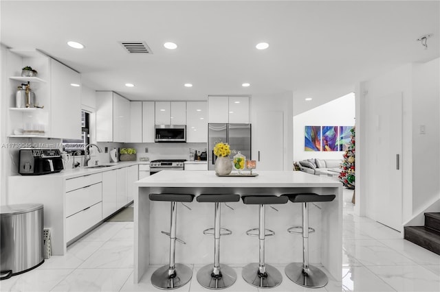 kitchen with sink, appliances with stainless steel finishes, white cabinetry, a center island, and a kitchen bar