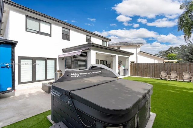 back of house featuring a hot tub, a patio area, and a lawn