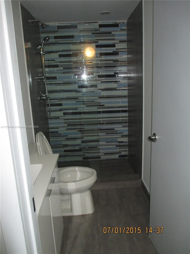 bathroom featuring tile patterned flooring, vanity, a tile shower, and toilet