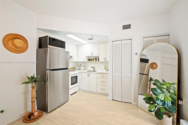 kitchen featuring white cabinetry, stainless steel fridge, sink, and white stove