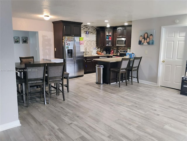 kitchen featuring decorative backsplash, dark brown cabinetry, stainless steel appliances, and a breakfast bar area