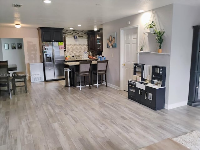 kitchen with stainless steel refrigerator with ice dispenser, a breakfast bar, backsplash, and light hardwood / wood-style floors