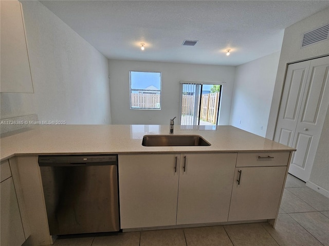 kitchen with light tile patterned flooring, sink, stainless steel dishwasher, kitchen peninsula, and a textured ceiling