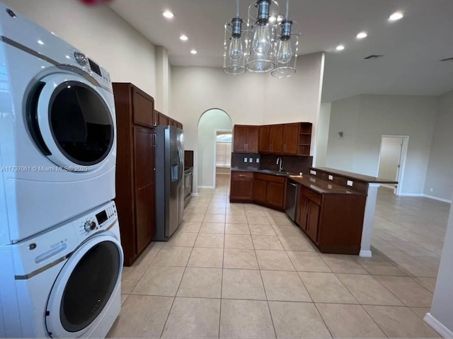 kitchen featuring appliances with stainless steel finishes, a towering ceiling, sink, stacked washer and clothes dryer, and light tile patterned floors