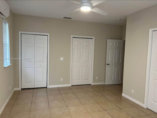 unfurnished bedroom with ceiling fan, an AC wall unit, light tile patterned floors, and two closets