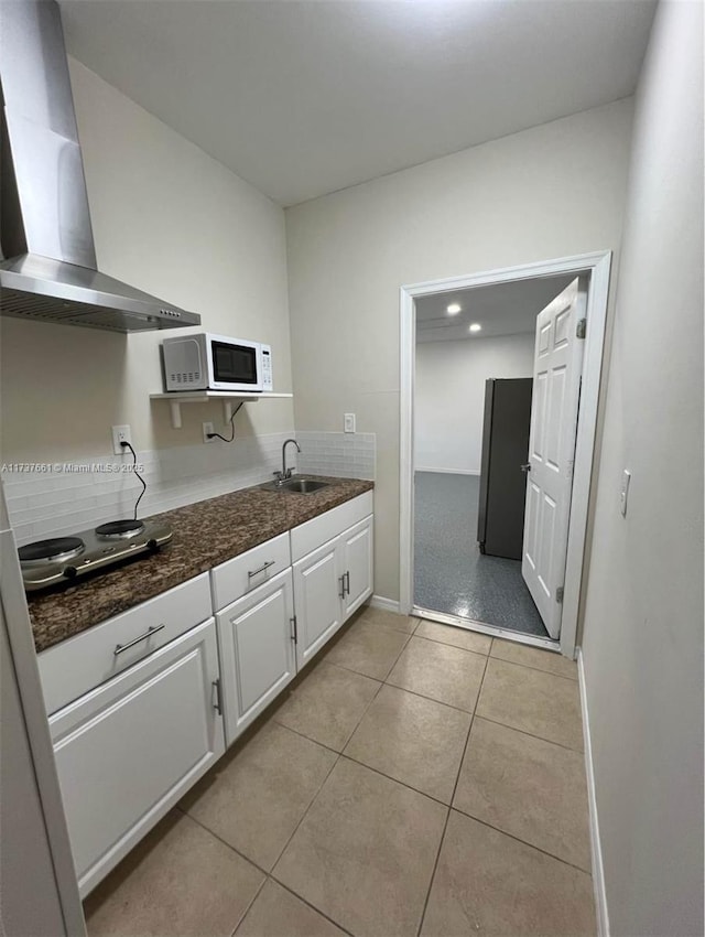 kitchen with stovetop, sink, light tile patterned floors, wall chimney range hood, and white cabinets