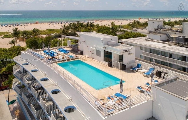 view of pool featuring a water view, a view of the beach, and a patio area