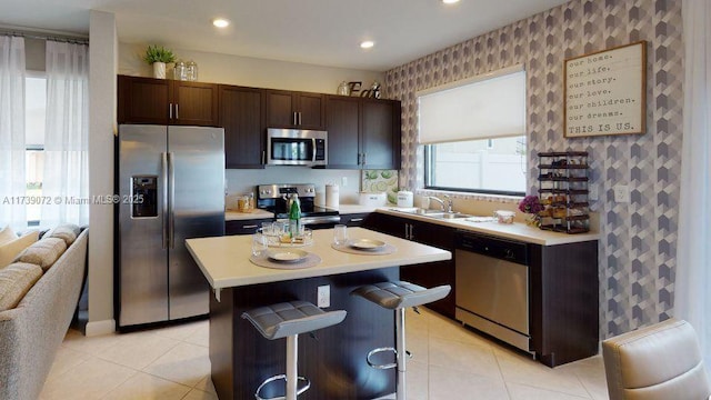 kitchen with a kitchen island, a breakfast bar, sink, stainless steel appliances, and dark brown cabinets