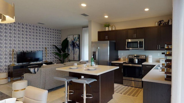 kitchen with a kitchen bar, dark brown cabinets, a center island, and appliances with stainless steel finishes