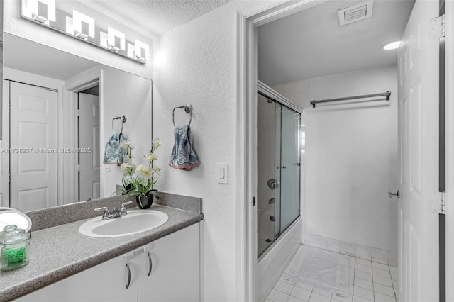 bathroom with tile patterned flooring, vanity, bath / shower combo with glass door, and a textured ceiling