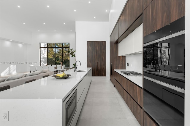 kitchen featuring light tile patterned floors, sink, white cabinetry, built in microwave, and a large island with sink