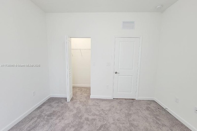 unfurnished bedroom with a spacious closet, light colored carpet, and a closet