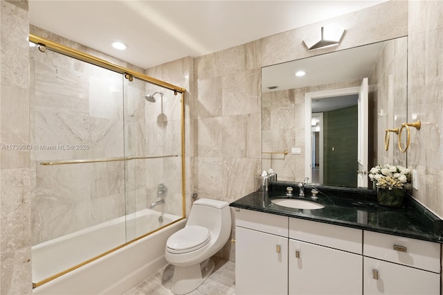 full bathroom with toilet, vanity, bath / shower combo with glass door, and tile walls