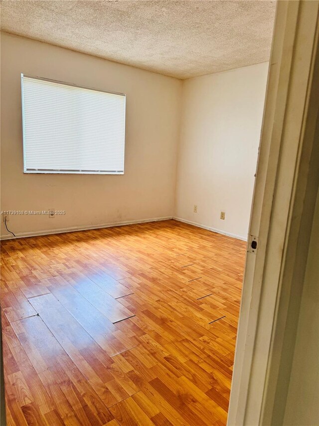 spare room with a textured ceiling and light hardwood / wood-style flooring