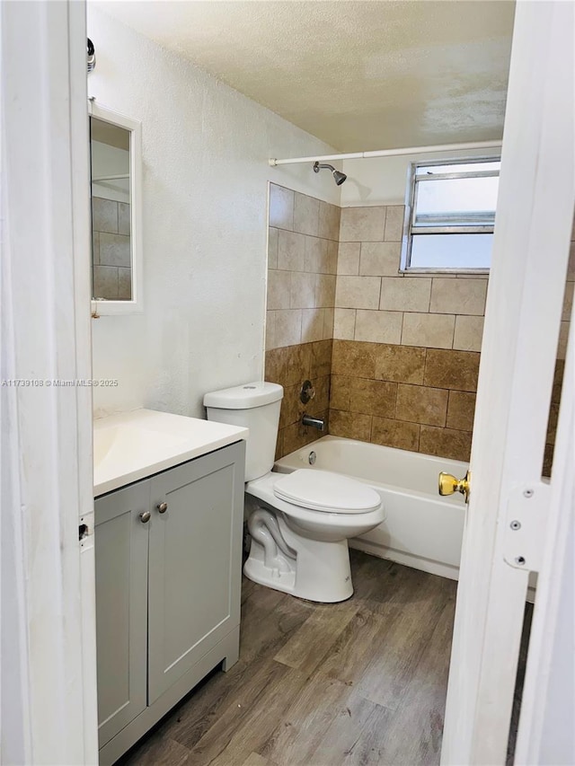 full bathroom featuring hardwood / wood-style flooring, tiled shower / bath combo, vanity, a textured ceiling, and toilet