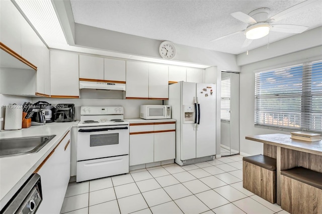 kitchen with sink, a textured ceiling, light tile patterned floors, white appliances, and white cabinets