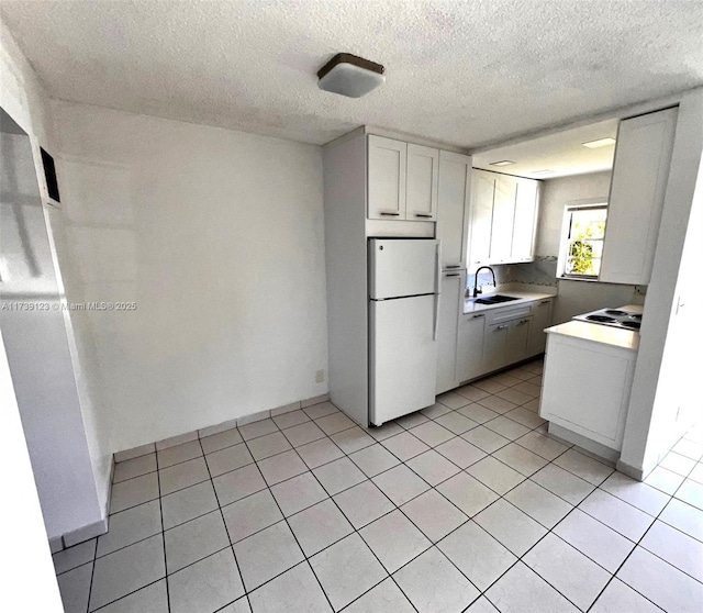 kitchen featuring light tile patterned flooring, sink, a textured ceiling, white refrigerator, and white cabinets