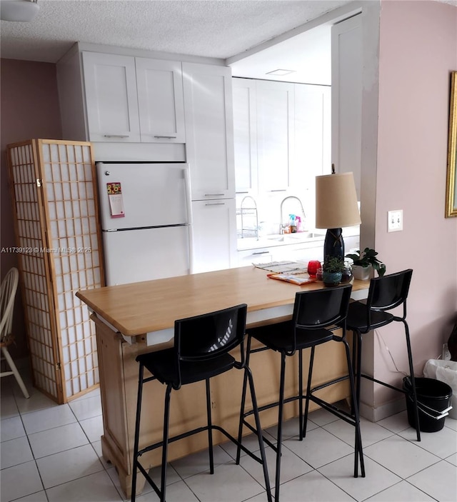 2145 Pierce St Unit 105, Hollywood, FL 33020 - kitchen with a textured ceiling, freestanding refrigerator, white cabinetry, and a breakfast bar