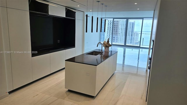 kitchen with pendant lighting, sink, white cabinets, and a center island with sink