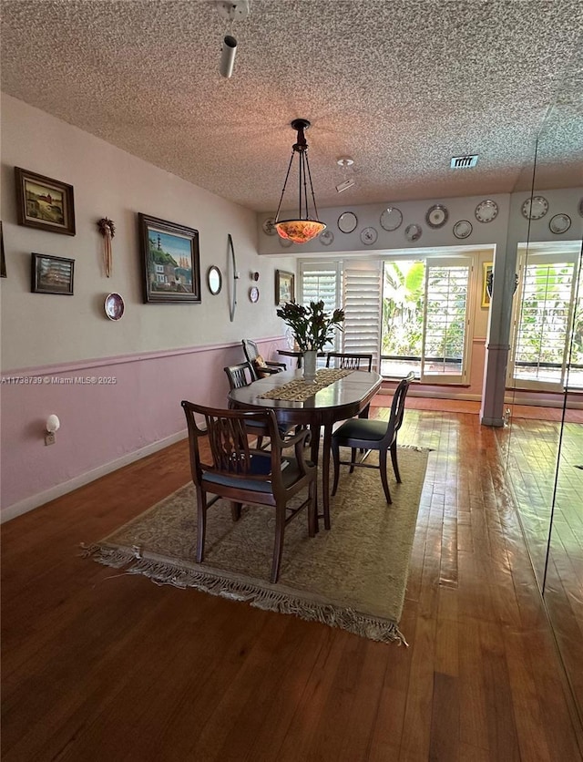 dining area with visible vents, a textured ceiling, baseboards, and hardwood / wood-style floors