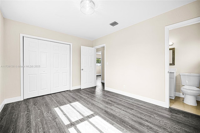 unfurnished bedroom featuring connected bathroom, dark wood-type flooring, and a closet