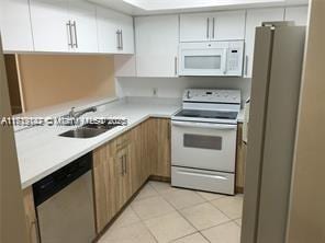 kitchen with appliances with stainless steel finishes, sink, light tile patterned floors, and white cabinets