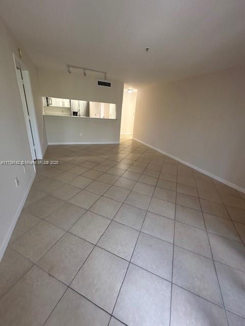 empty room with light tile patterned floors, track lighting, visible vents, and baseboards