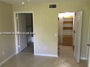 unfurnished bedroom with light tile patterned flooring, visible vents, baseboards, a closet, and a walk in closet