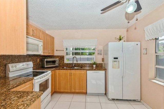 kitchen with sink, white appliances, dark stone counters, and light tile patterned flooring