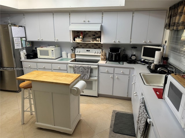 kitchen featuring a kitchen bar, sink, light tile patterned floors, a kitchen island, and white appliances