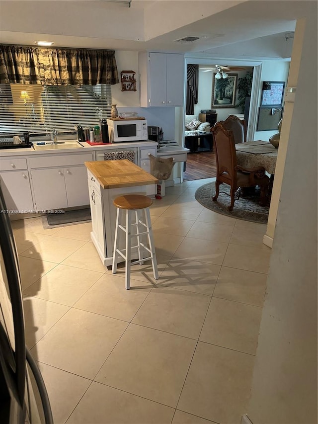 kitchen featuring sink, white cabinets, a kitchen bar, light tile patterned floors, and ceiling fan