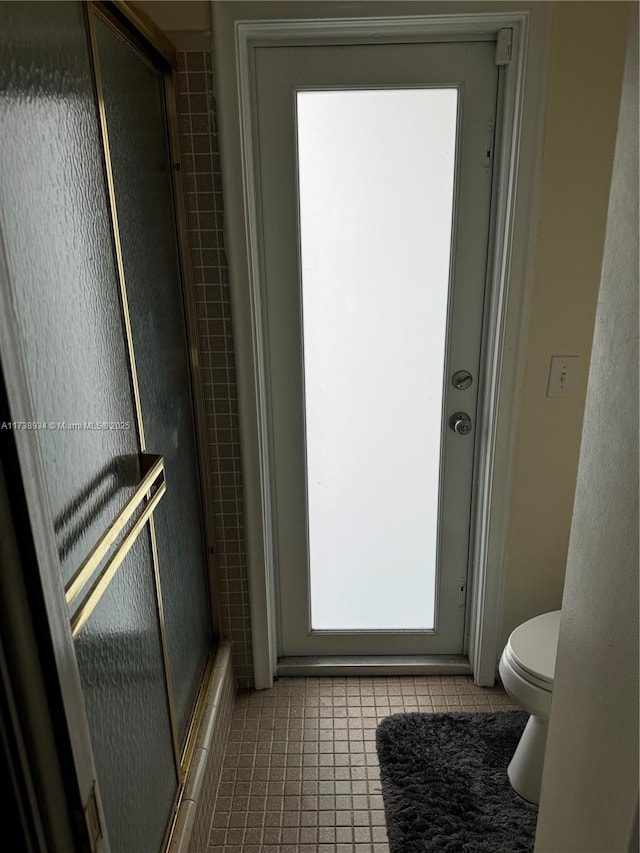 bathroom featuring tile patterned floors, toilet, and a shower with shower door